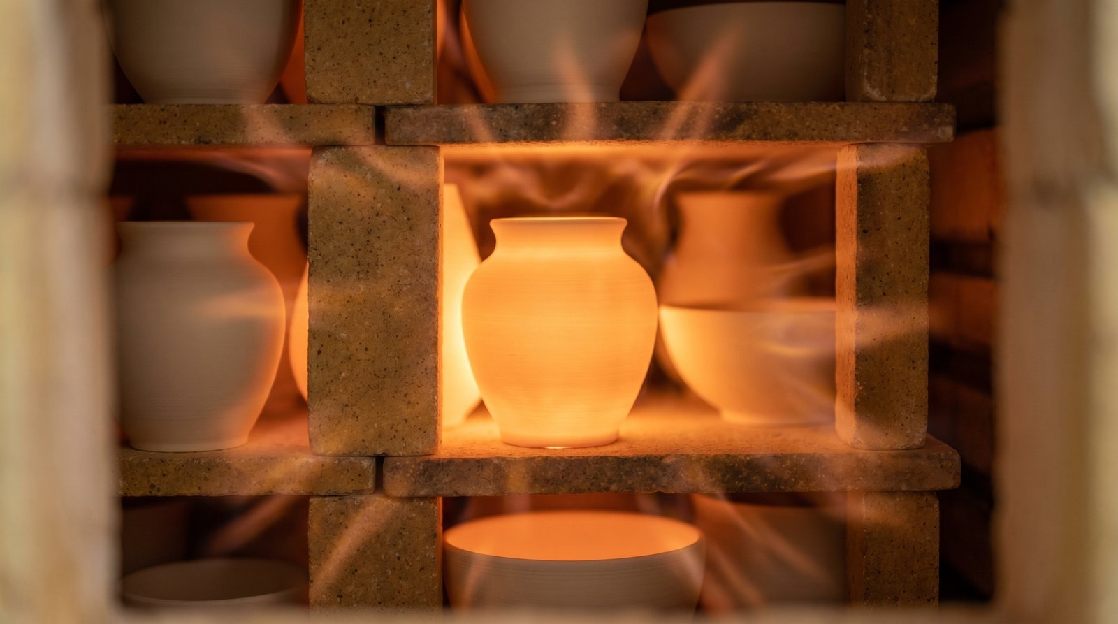A pottery kiln interior during firing showing bisque-fired ceramic pieces glowing in the heat