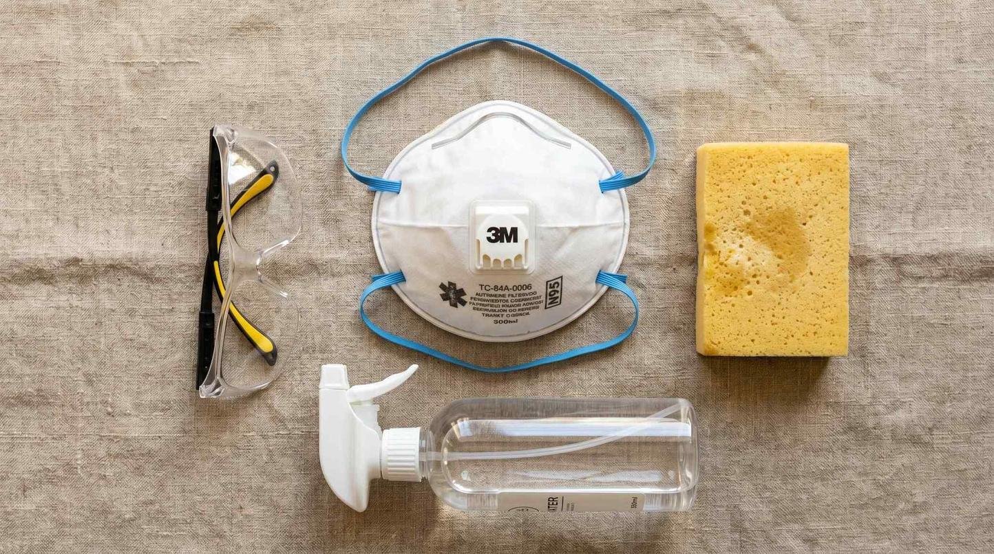 Pottery safety equipment flat lay showing N95 respirator mask, safety glasses, wet sponge and spray bottle for dust suppression