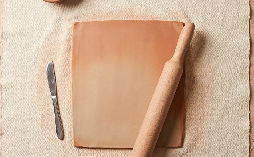 Clay slab rolled flat on canvas with rolling pin and fettling knife, showing the slab pottery technique setup