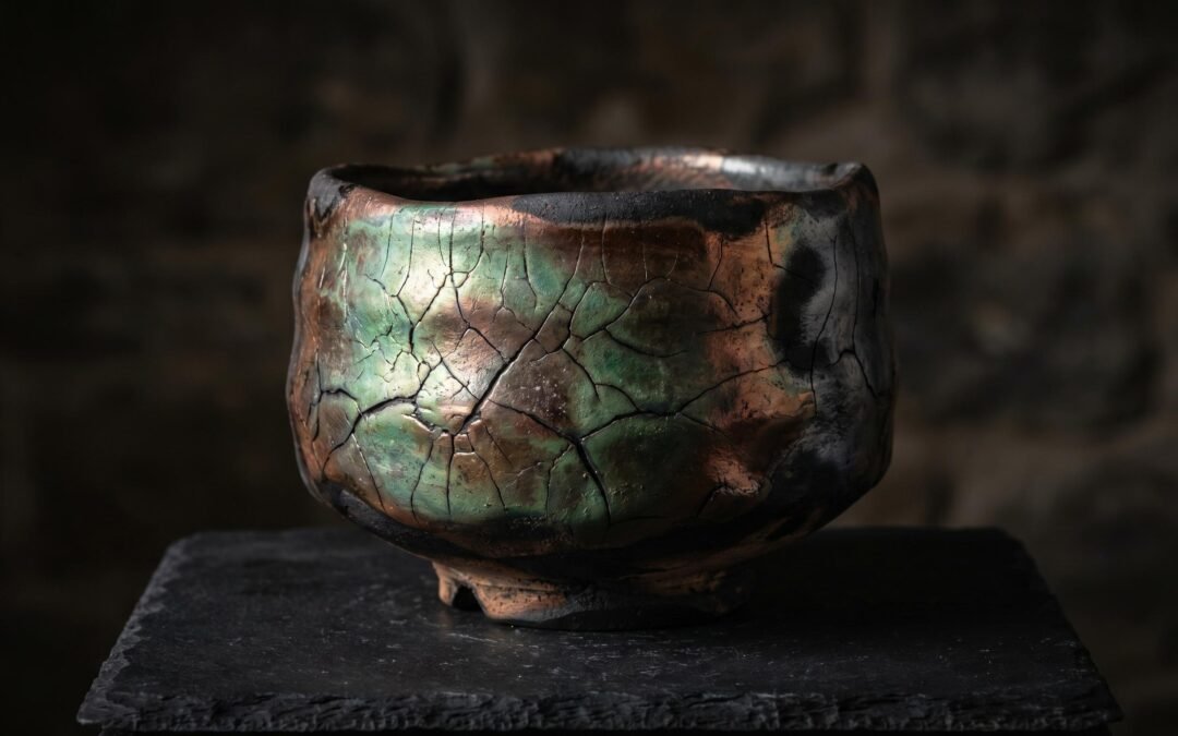 Raku pottery tea bowl with copper matte glaze showing iridescent green metallic tones and crackle patterns